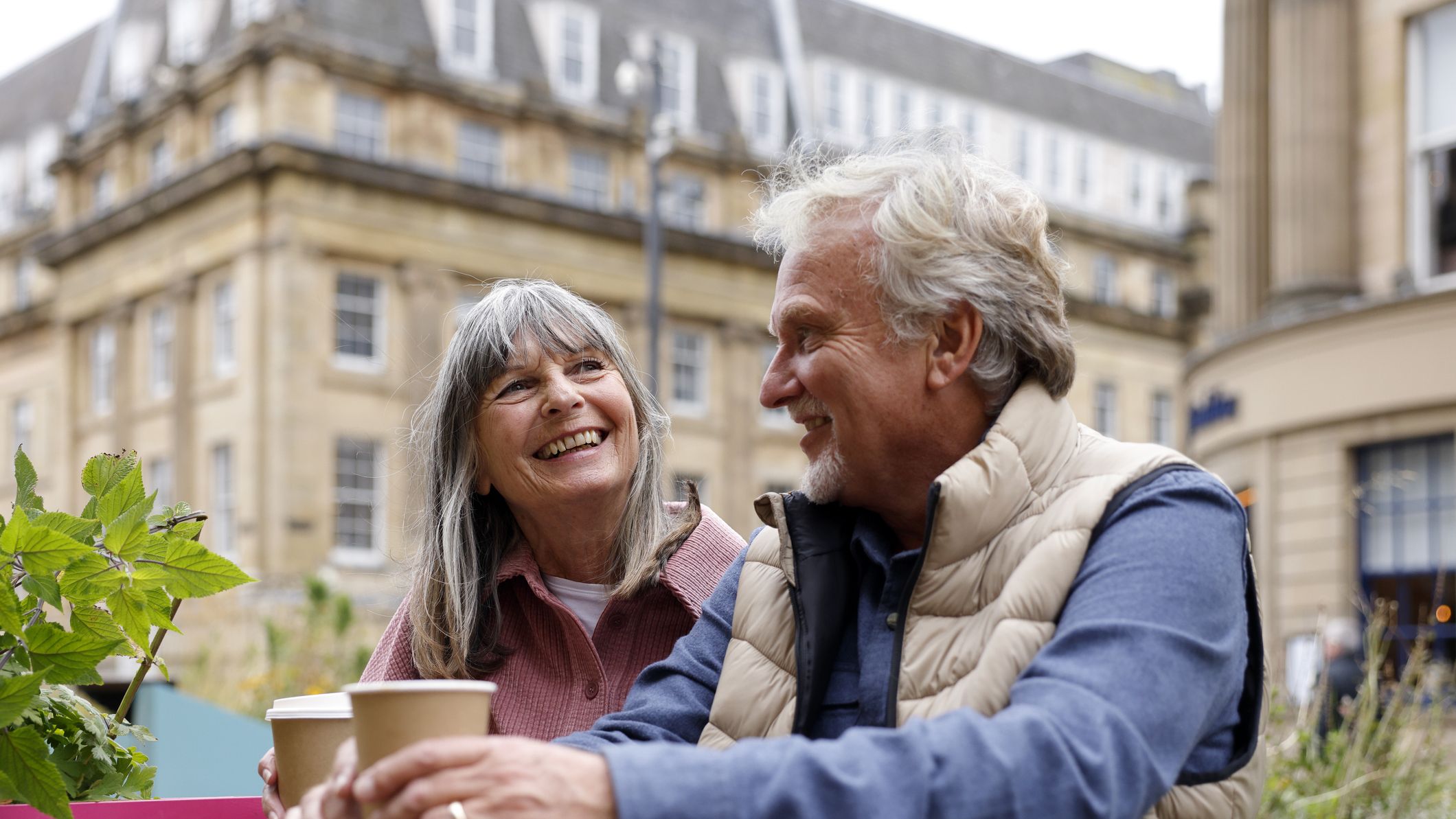 A happy senior couple enjoy a moment together while seated at an outdoor city caf&eacute; during a city break. The scene captures companionship, relaxation and the pleasure of exploring a new destination together.