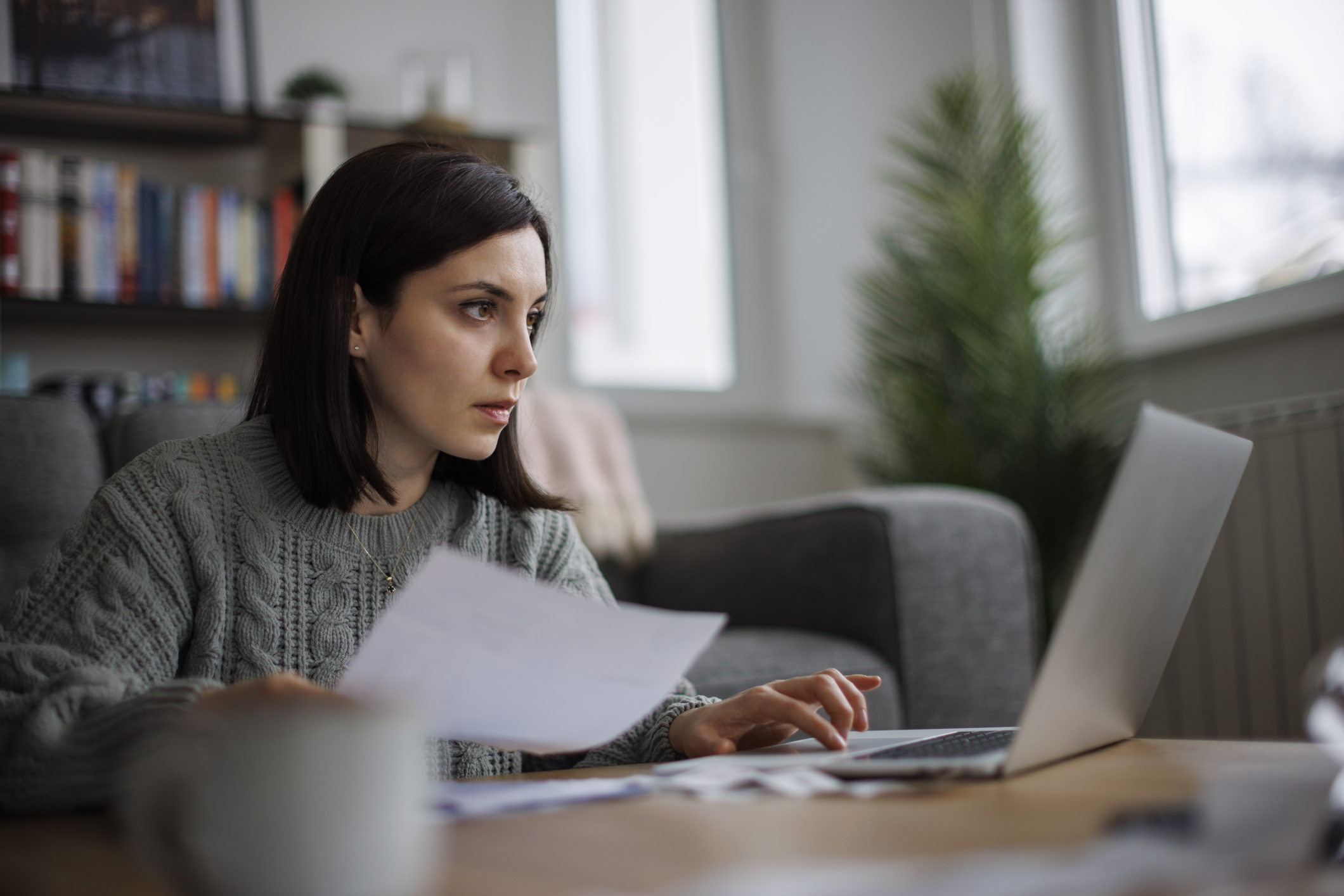 Woman Checking Paperwork On Laptop At Home