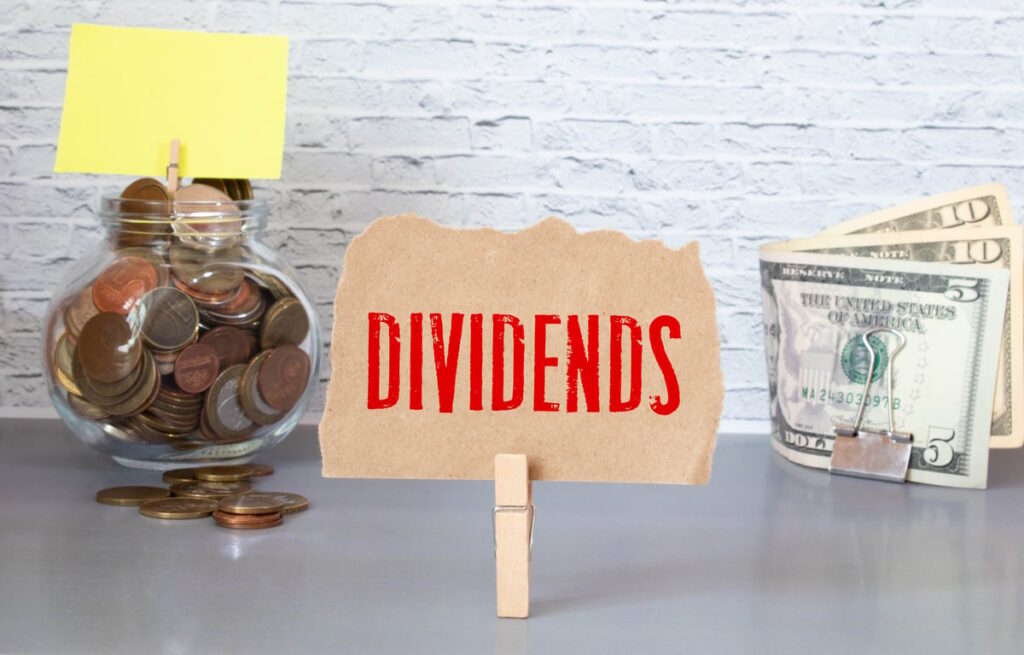 Paper sign with the word "Dividends" clipped to a stand, with cash in the background.