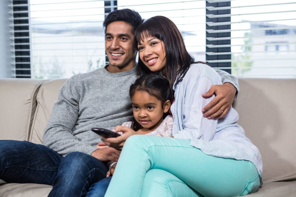 Three people sitting on a couch watching TV.