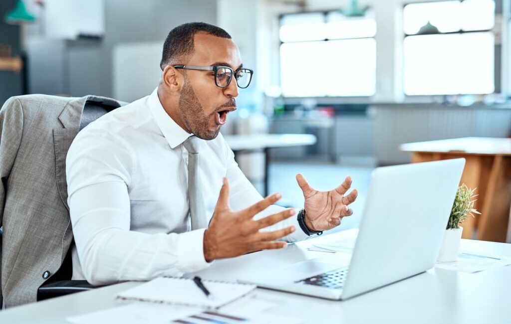 An excitedly-happy person is sitting at a desk in front of a laptop.