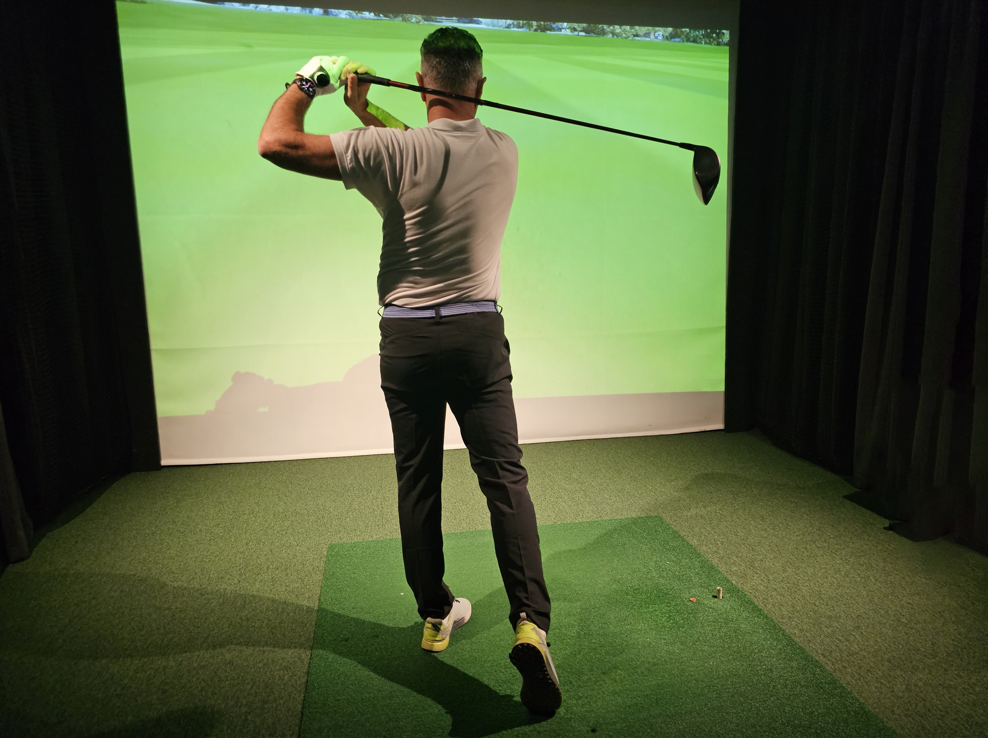 Professional male golfer holding club playing golf indoors on golf simulator
