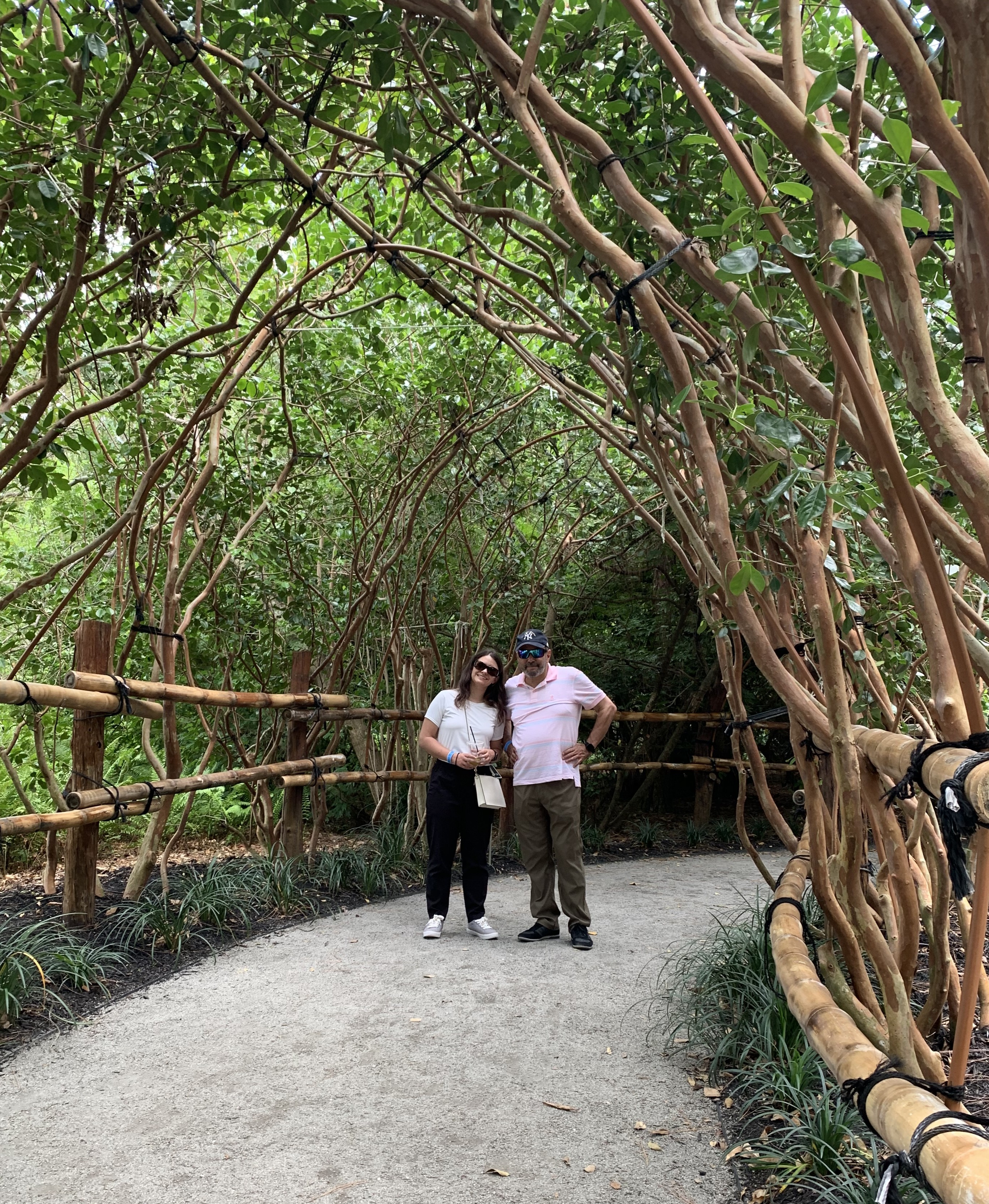 A woman and her father smile in a tree-lined path at a park.