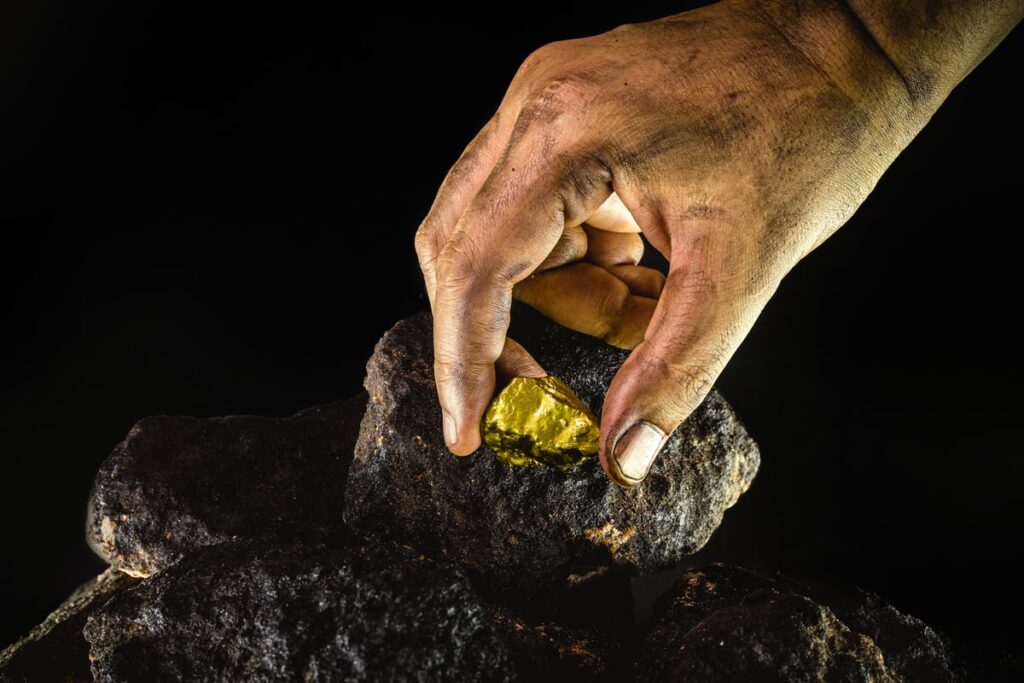 A miner's hand removing a gold nugget from a rock.