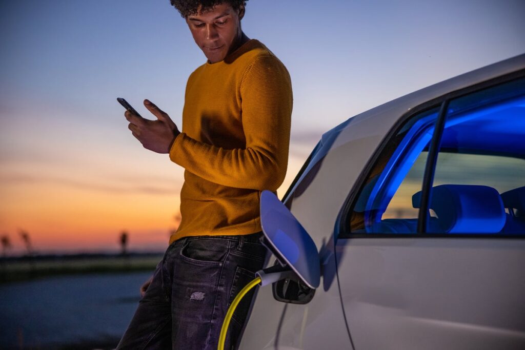 A person uses a smartphone while charging an electric car.