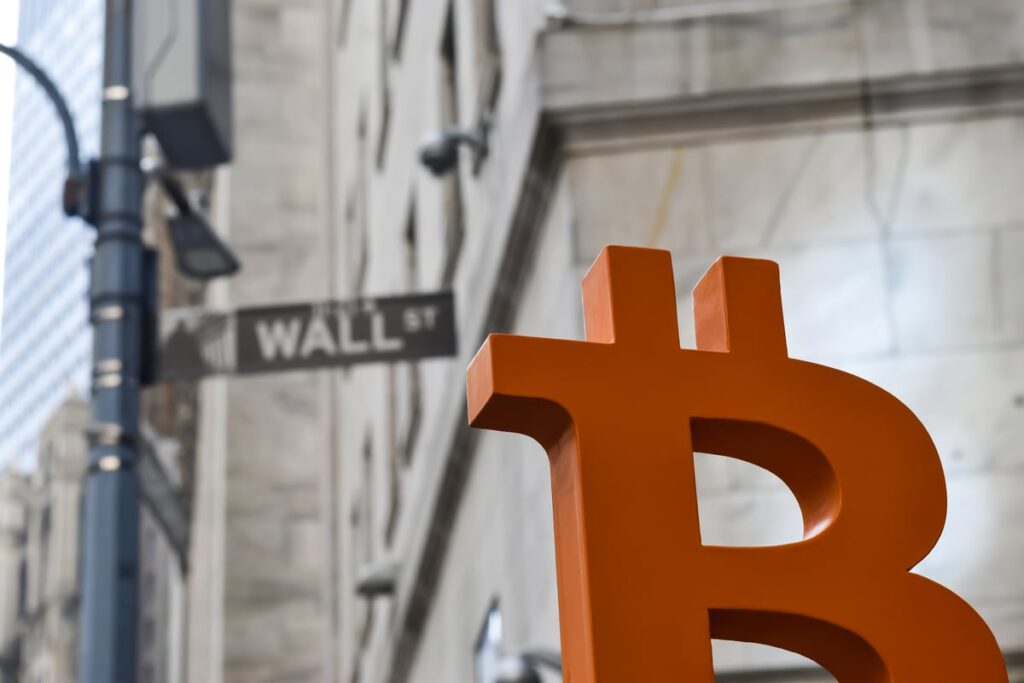 A Bitcoin logo looms in front of the street sign for Wall Street.