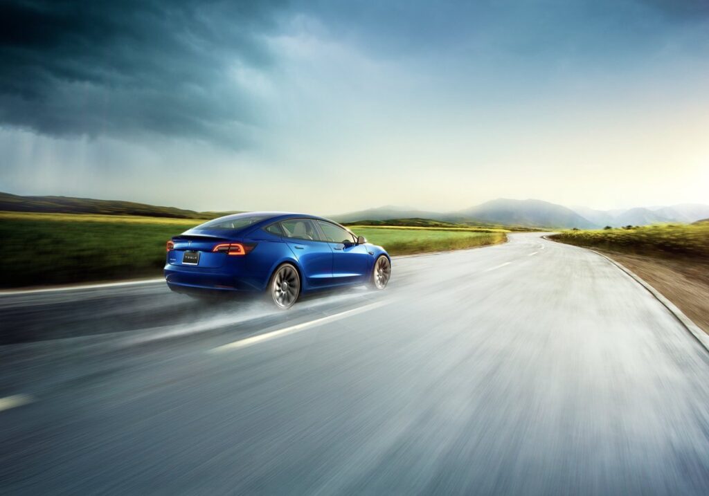 A Tesla car driving fast through the rain on an open road.