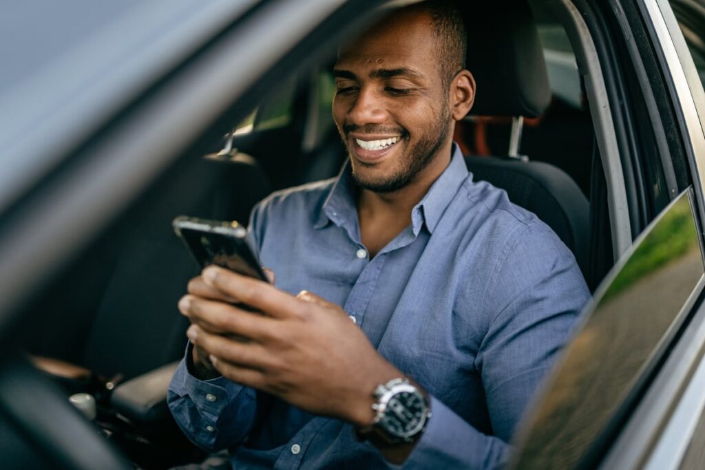 Person in car smiling while gazing at a smartphone.