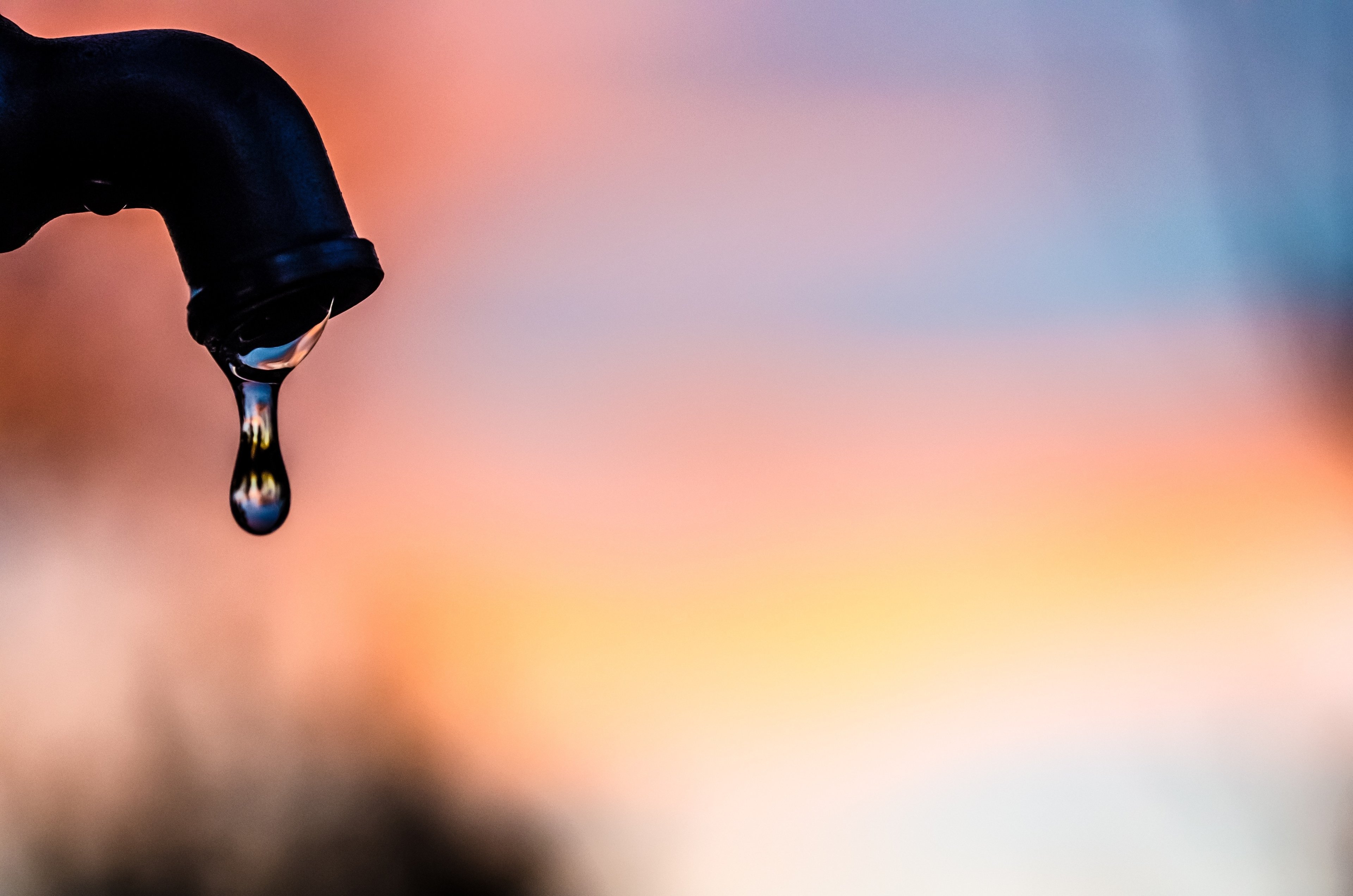 A water droplet falling from an outdoor spigot at twilight. 