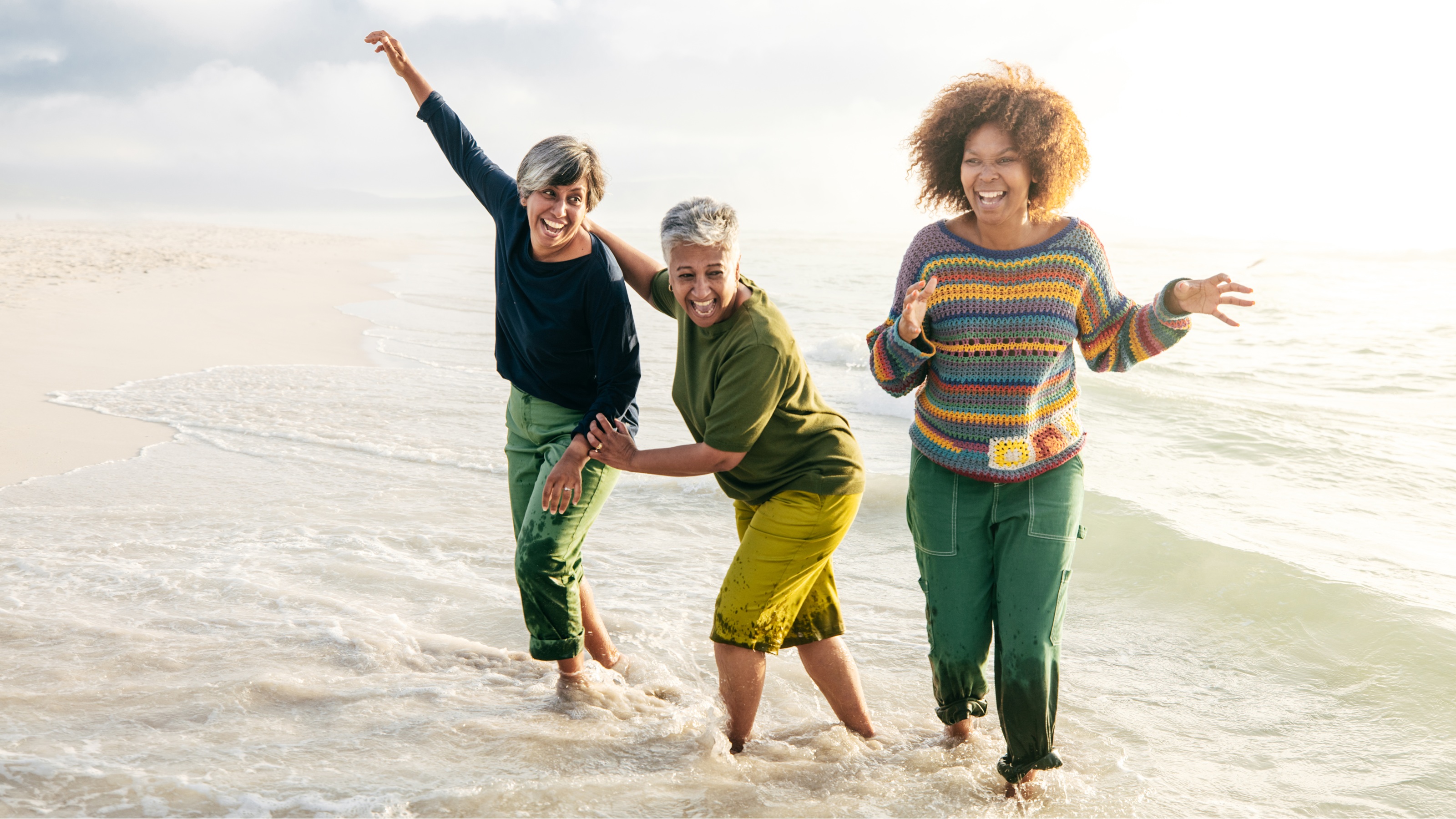 Three older women laugh and have fun on the beach.