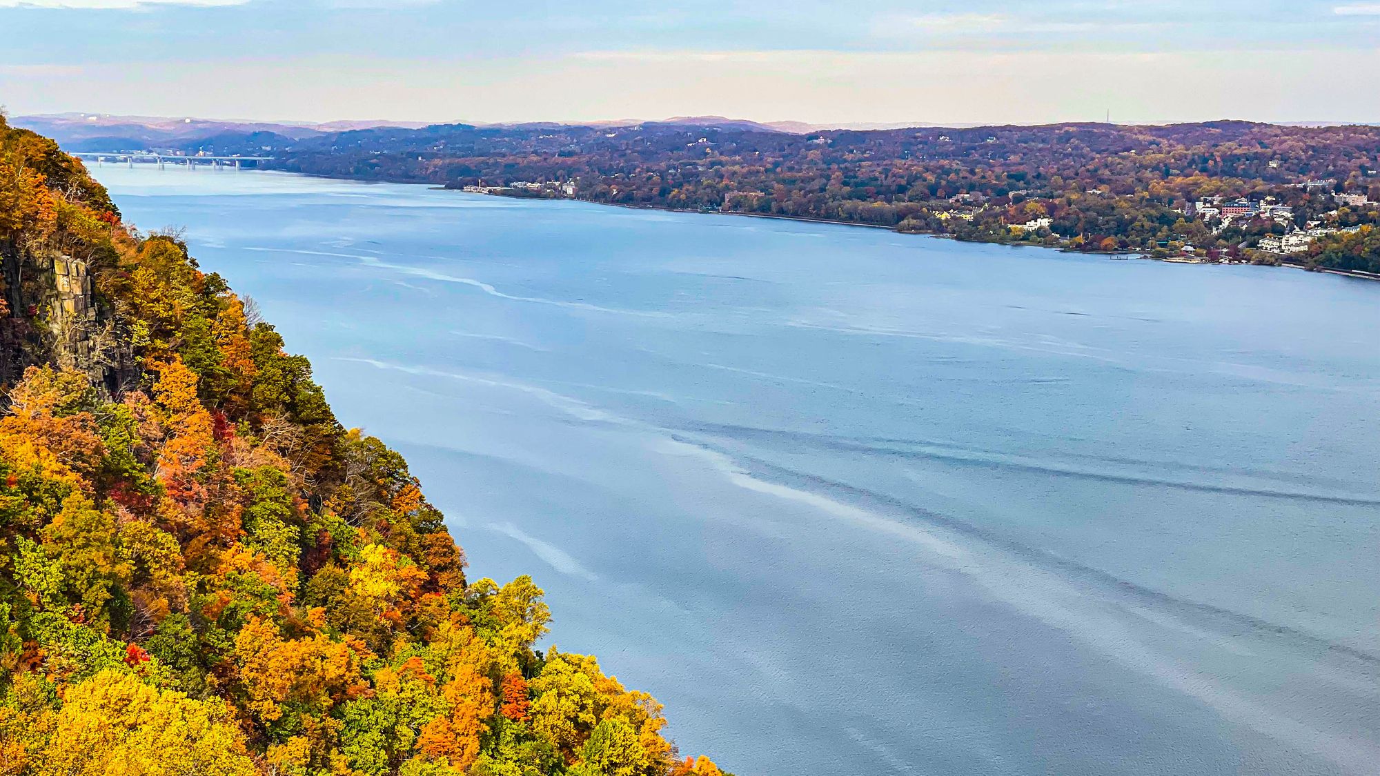 View of green, gold and orange leaves on trees below the Palisade cliffs adjoining the Hudson River below dramatic sky at state line lookout, Alpine, New Jersey, USA.