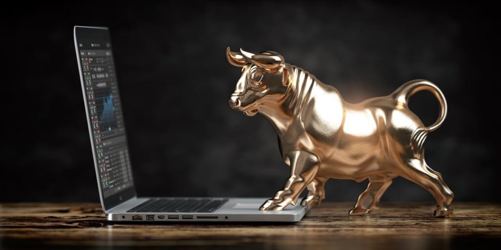 A golden bull facing a laptop with stock charts on it.