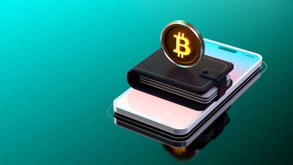 A Bitcoin stands on top of a wallet that's perched on top of a phone.