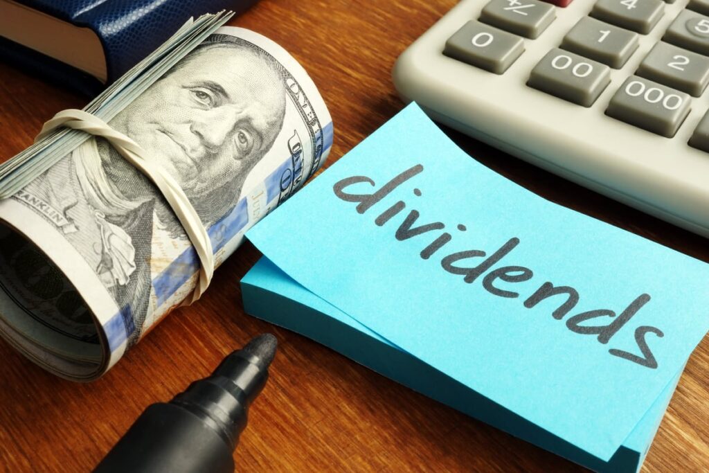 Rolled up money next to calculator and dividends written on post-it.
