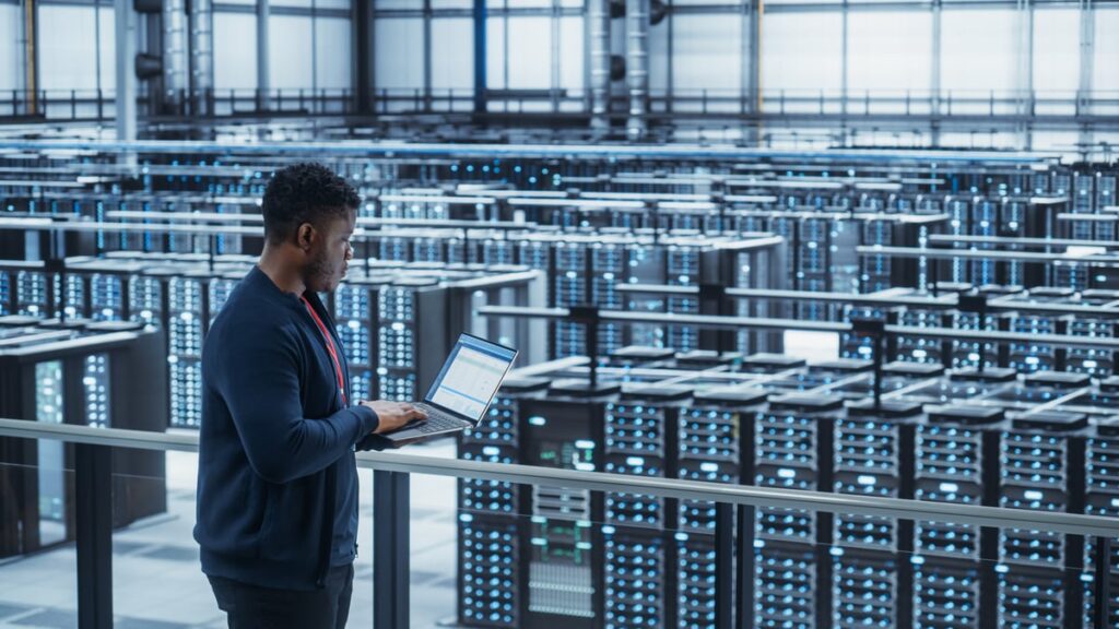 Person standing in a data center holding a laptop.