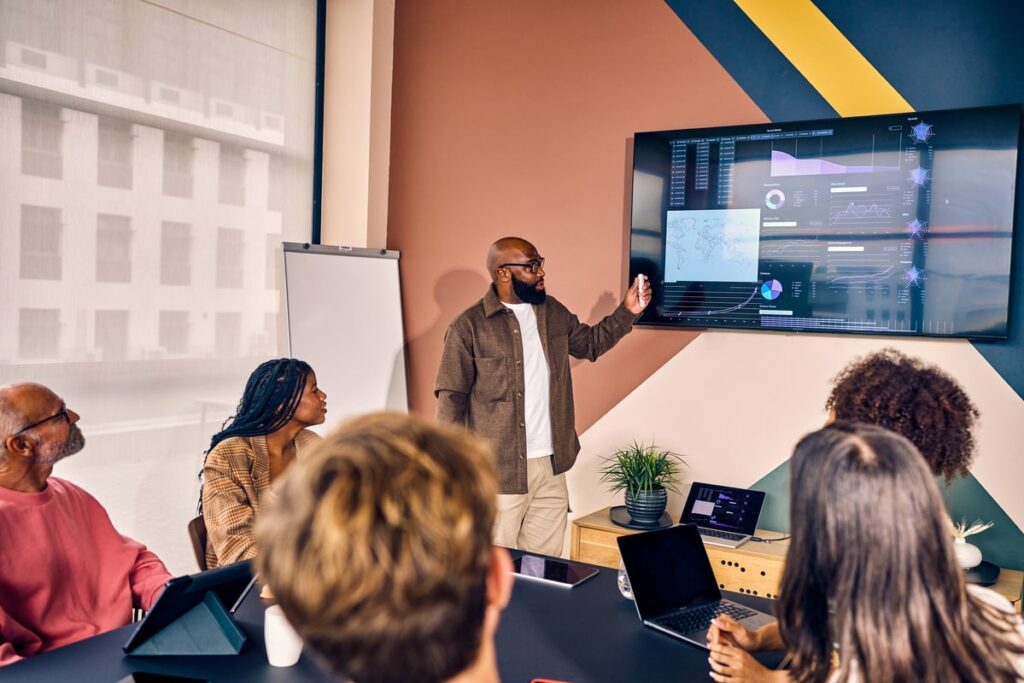 A group of people at a business presentation looking at charts on a TV.