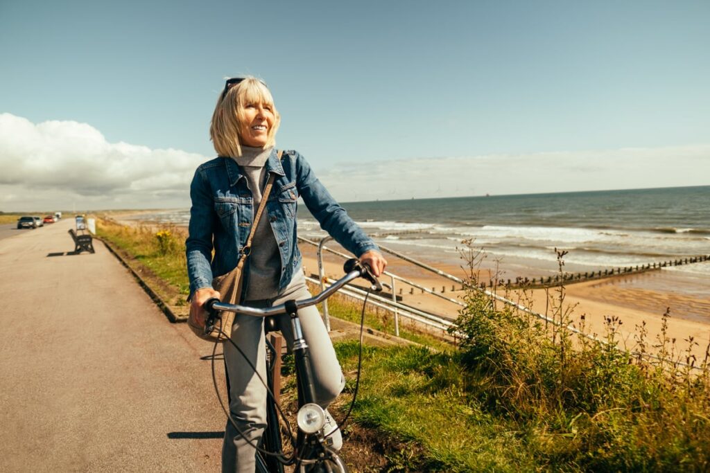 Smiling person riding bicycle by the ocean.