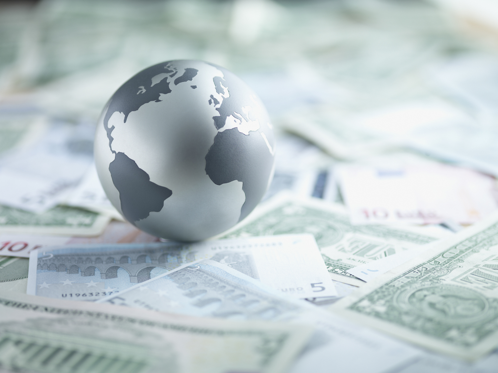 metal globe sitting on currencies from around the world