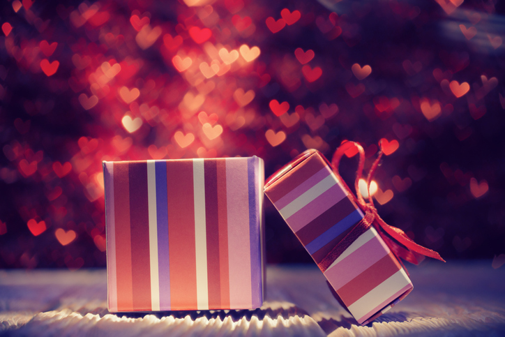 a pink, white and blue striped gift box with the lid off and red hearts coming out of it