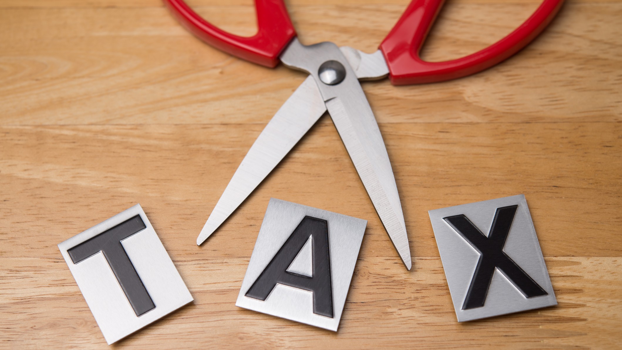 a pair of scissors with red handles placed above three silver blocks that spell out the word "TAX"