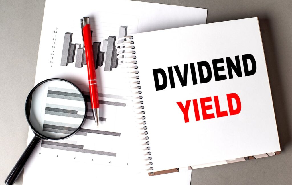 Dividend yield written on notebook next to charts, pen, and magnifying glass.