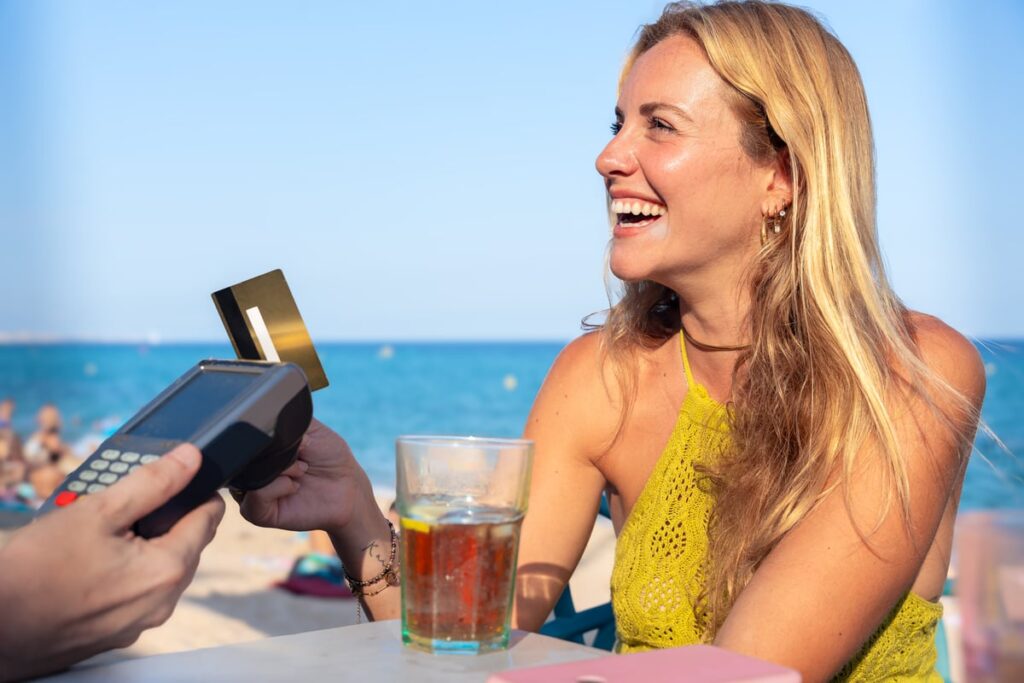 A person, smiling, eating outdoors, and paying for drinks with a credit card.