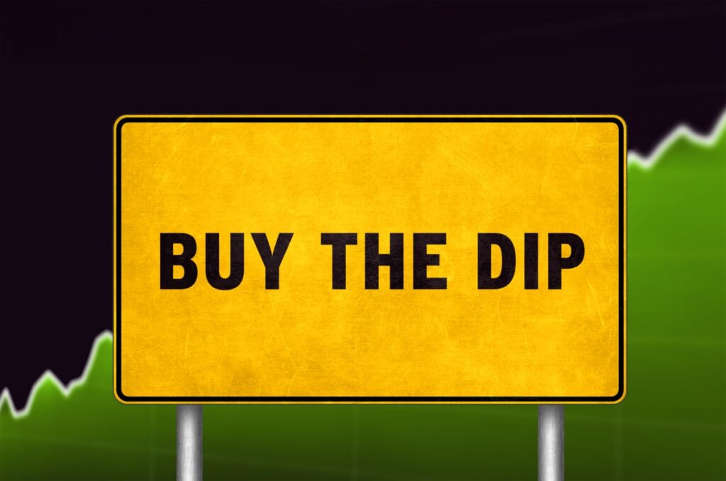 A sign that says Buy the Dip, with a stock chart in the background.