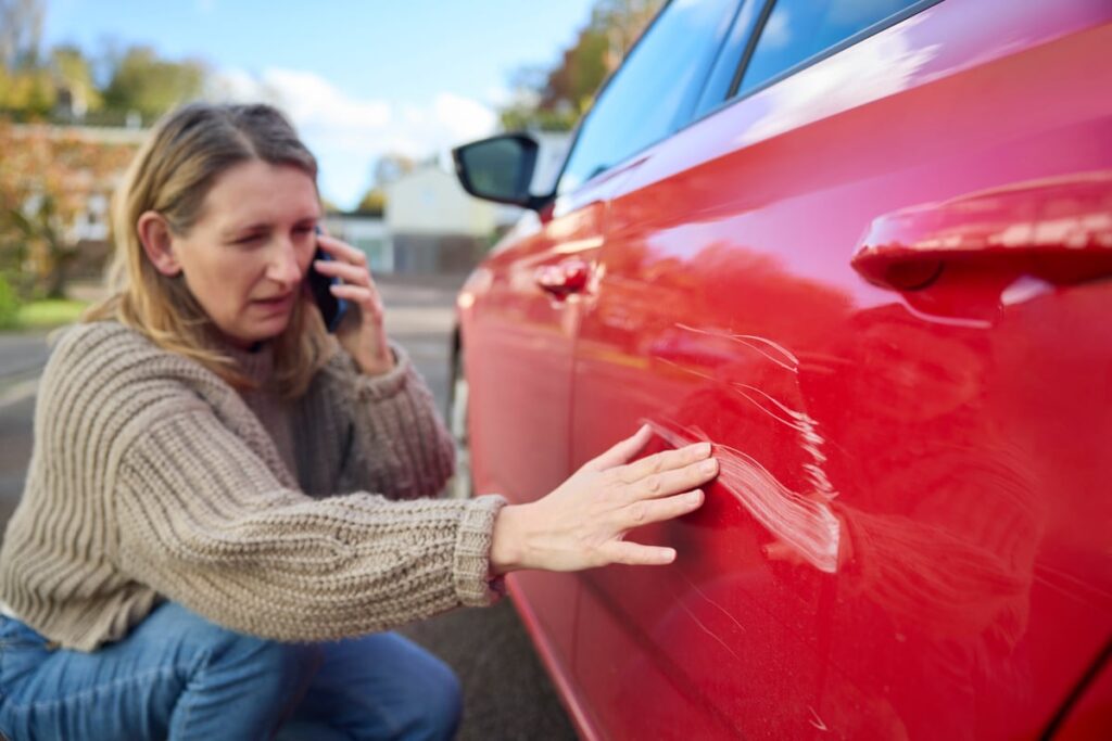 A person inspects damage to a car, while on the phone with an auto insurance provider.