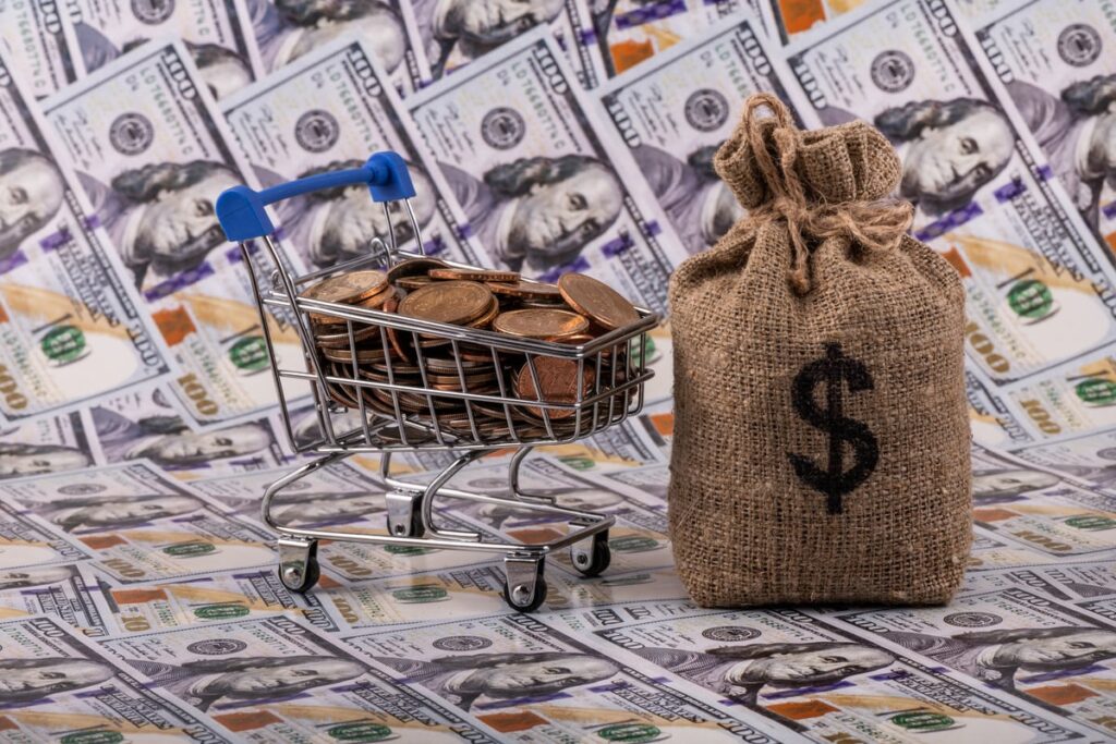 A cart filled with pennies next to a money back on top of $100 bills.