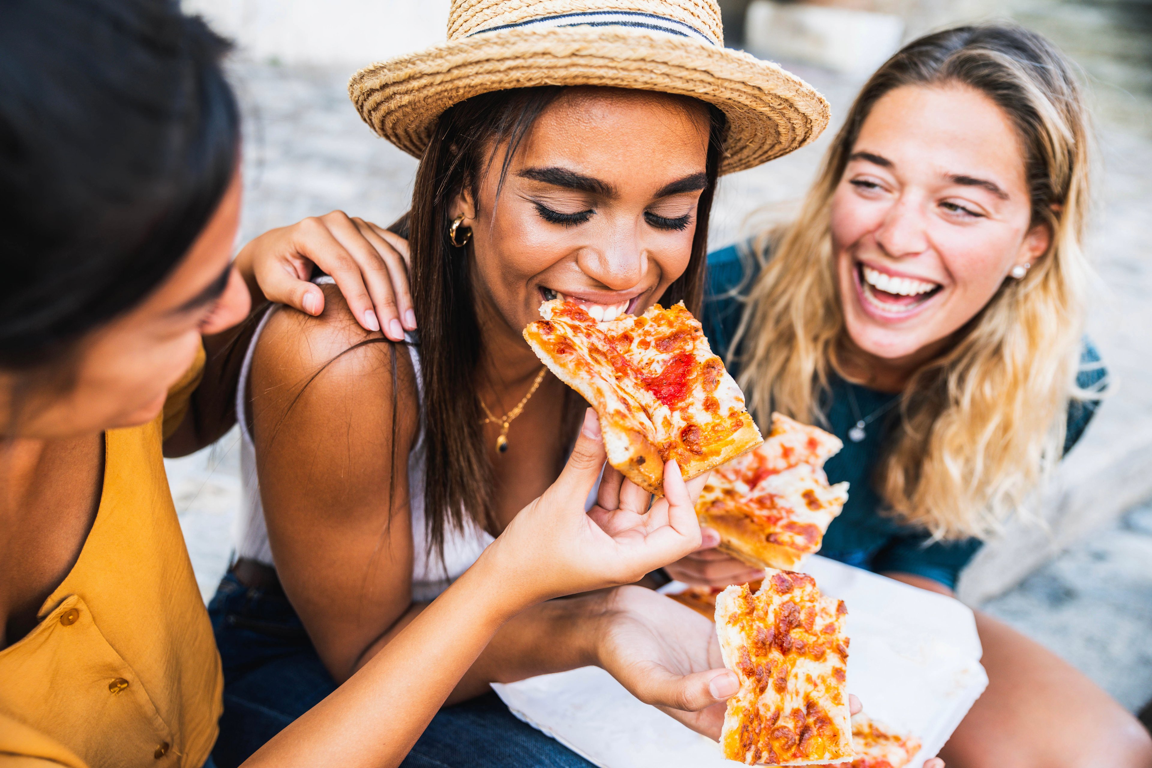 Three women happily eat pizza together.