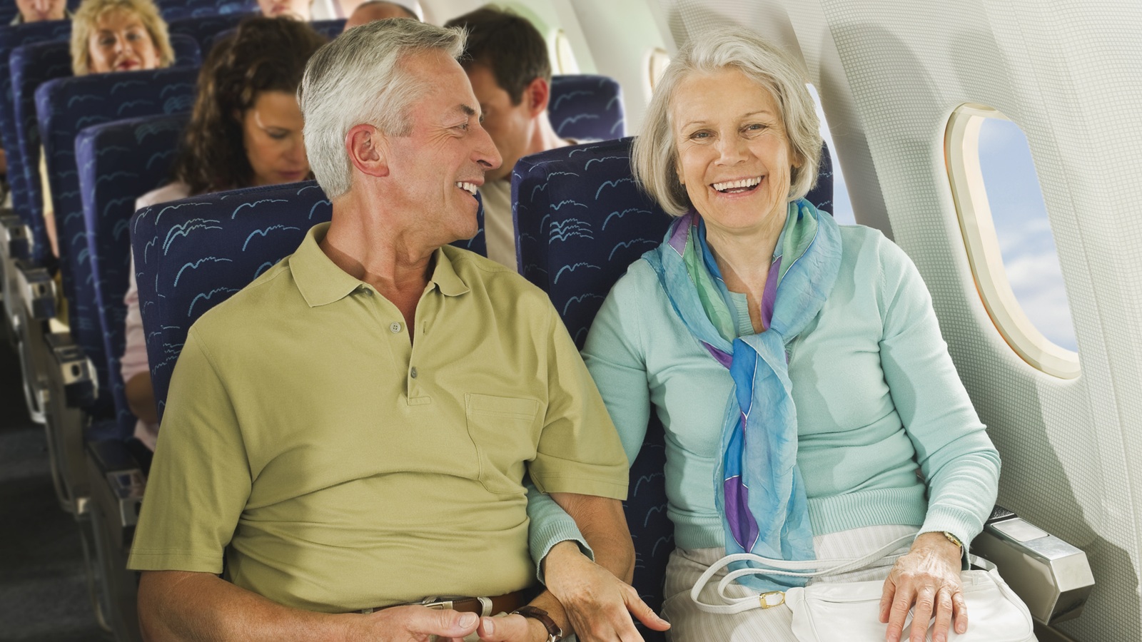 Mature couple on a plane, sitting arm-in-arm.