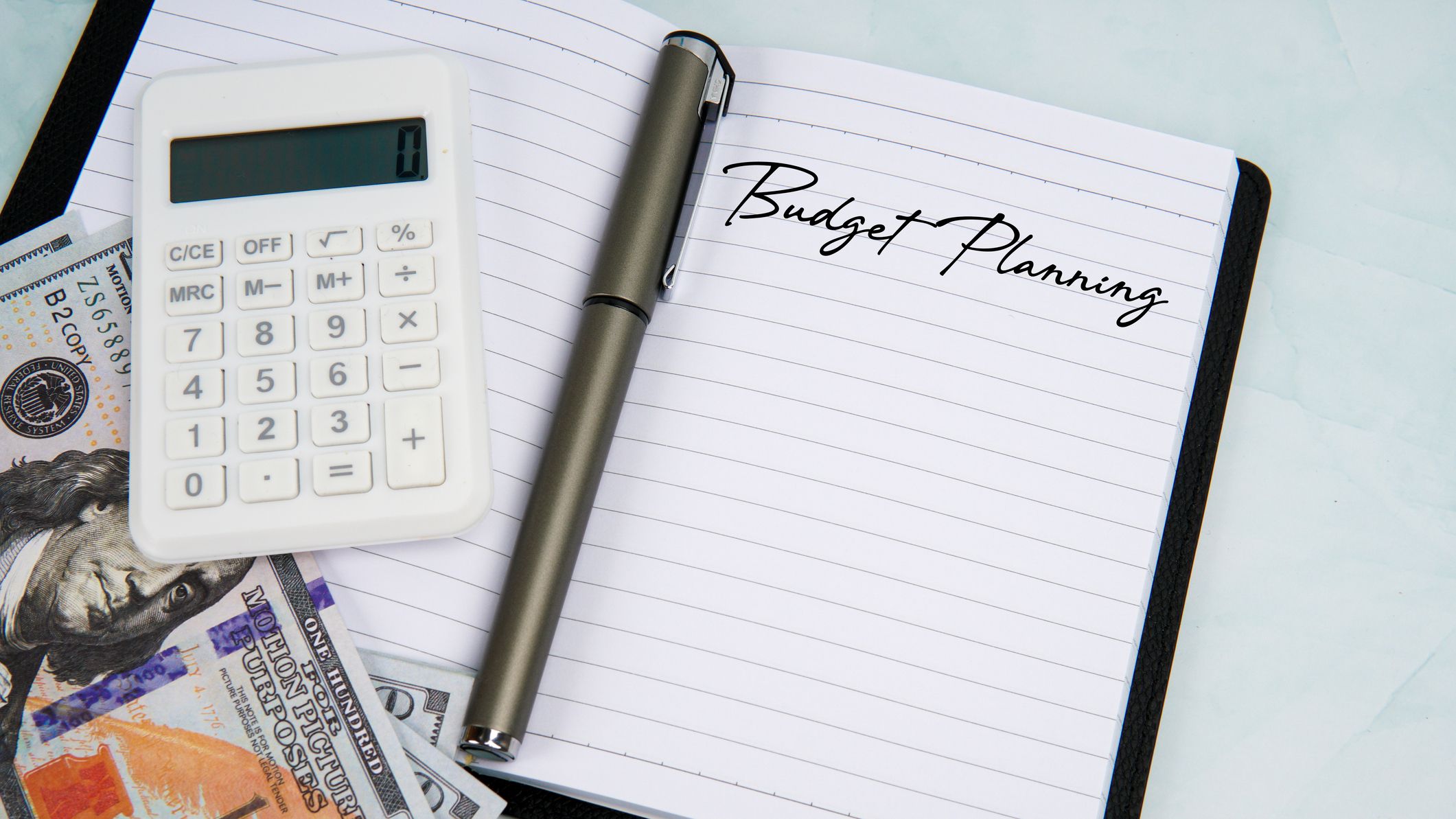 Notebook with Budget Planning text beside calculator, pen, and US dollar bills