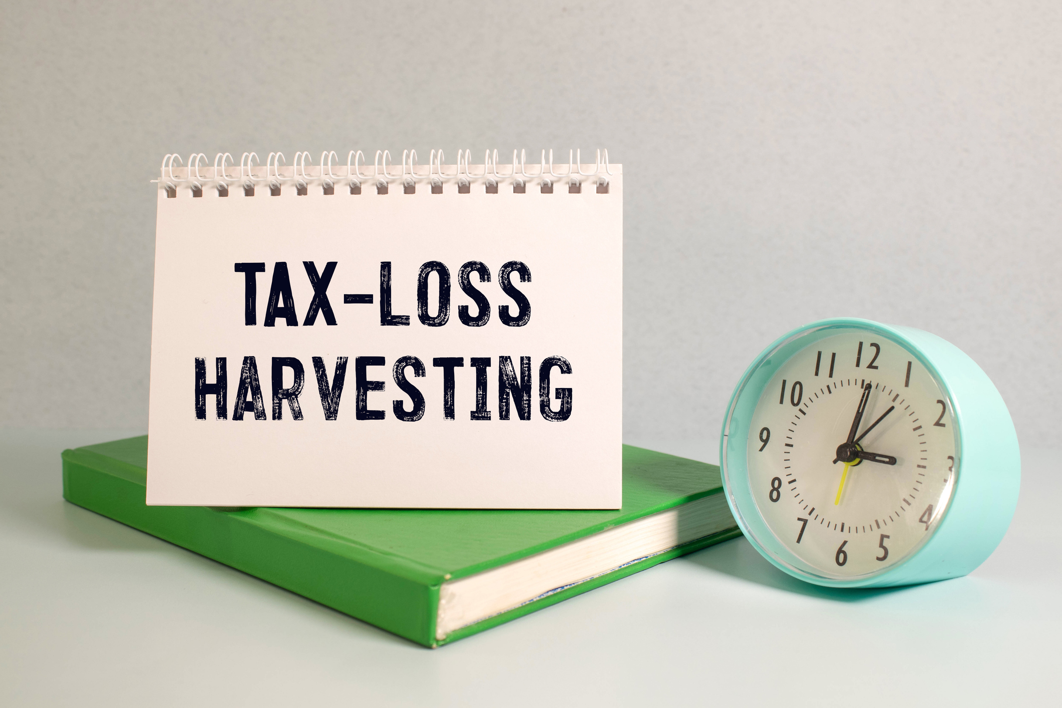 The words "Tax loss harvesting" on a notebook standing on a green book with a clock nearby