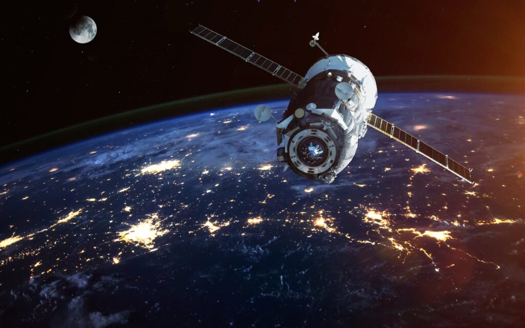 A satellite floats in space at night with the moon in the back.