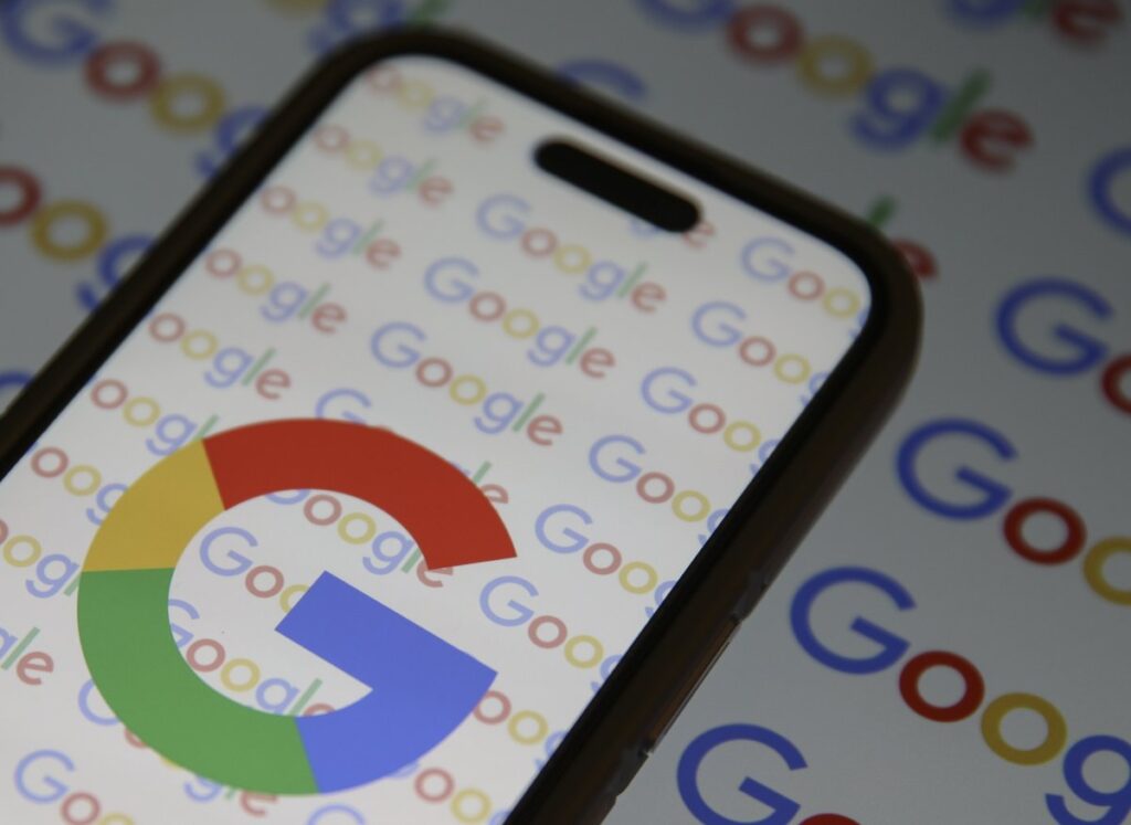 A phone displaying the big G Google logo with the word Google repeated in the background.