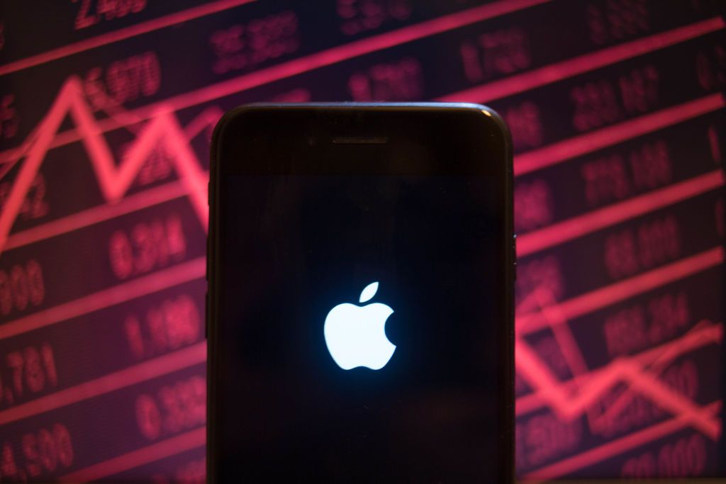 Apple logo displayed on an iPhone screen with a background of a market value dropping on the stock exchange behind.