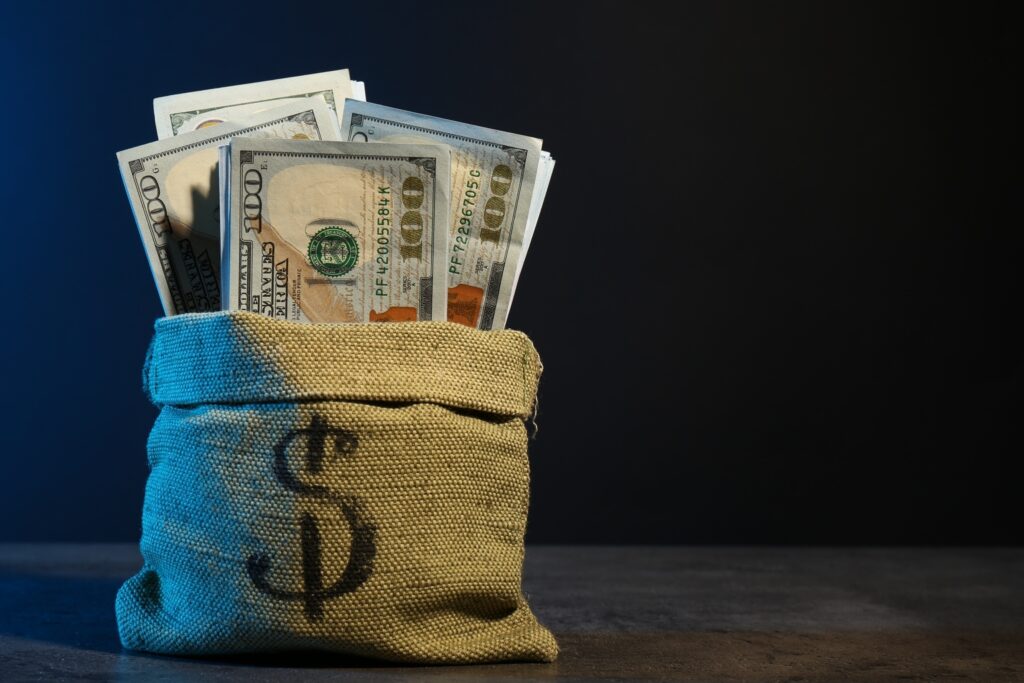Dollar banknotes in burlap sack on grey table against dark background in neon lights, space for text