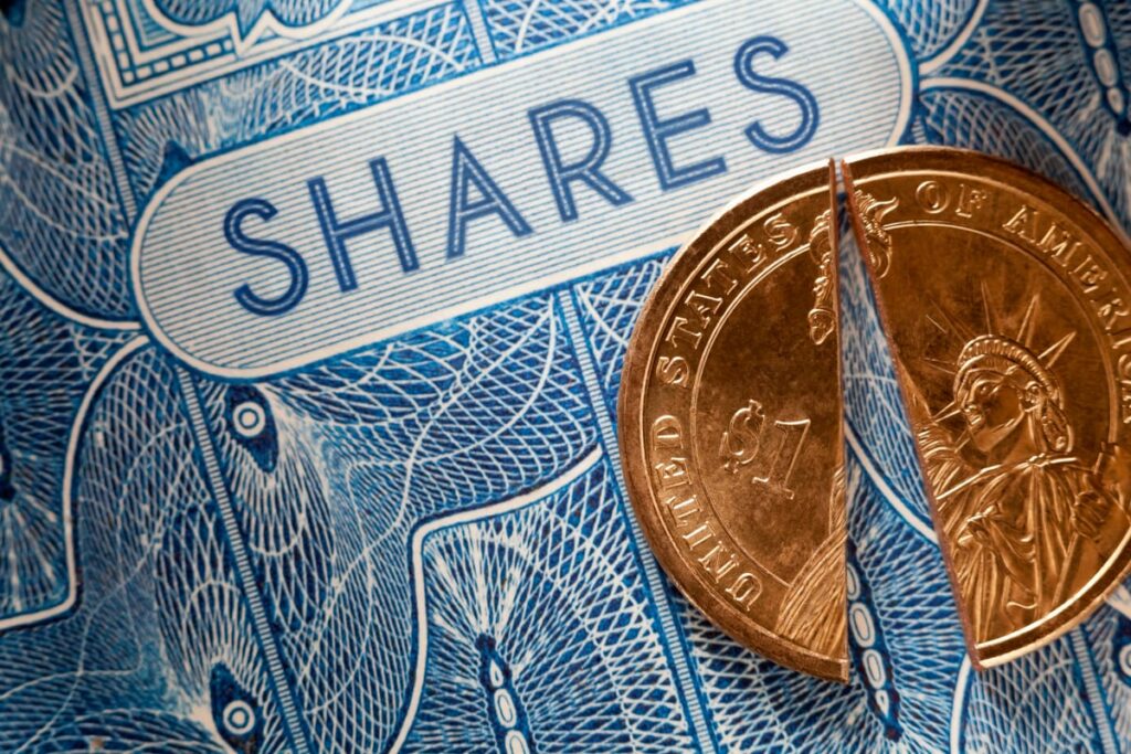 A U.S. $1 coin being cut in half over a stock certificate, illustrating the impact of stock splits.