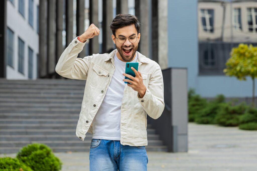 A person celebrates while looking at a smartphone.