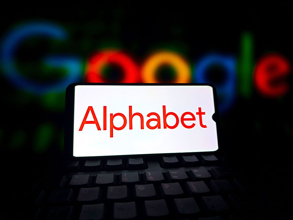 Alphabet logo displayed on a smartphone screen with Google script in the background
