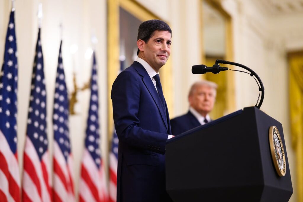 The new Federal Reserve Chairman Warsh stands at a podium during a press conference.