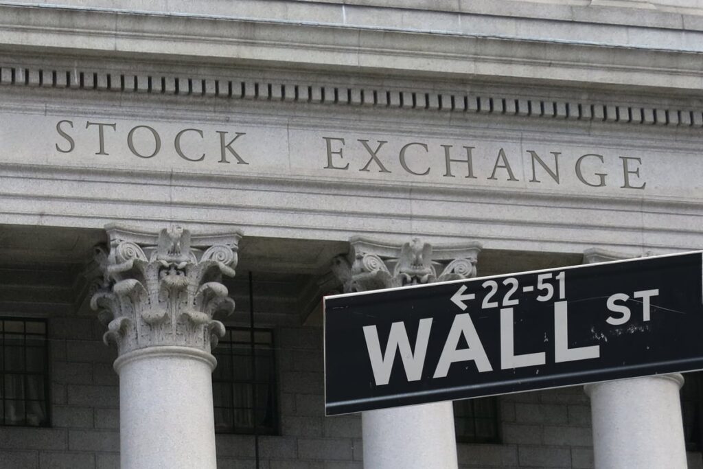 Street sign reading Wall St in front of a building with the words Stock Exchange carved above the columns.