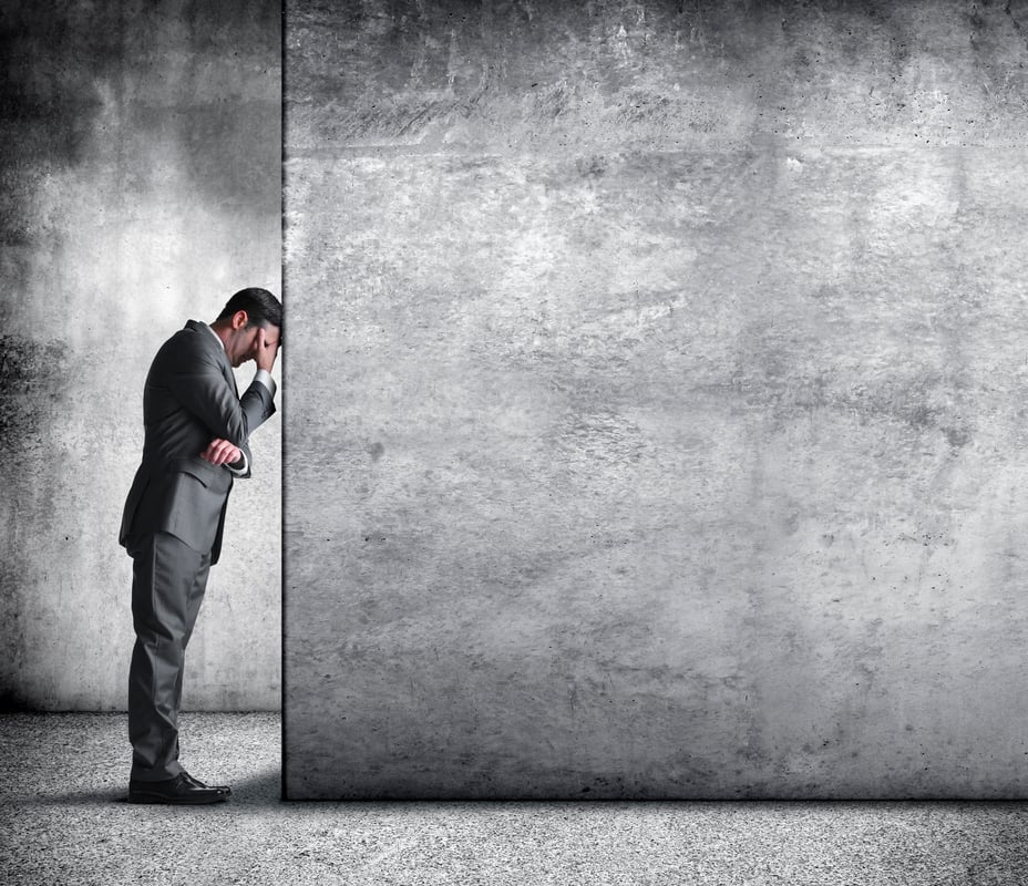 A person in a suit with their head against a wall in worry.