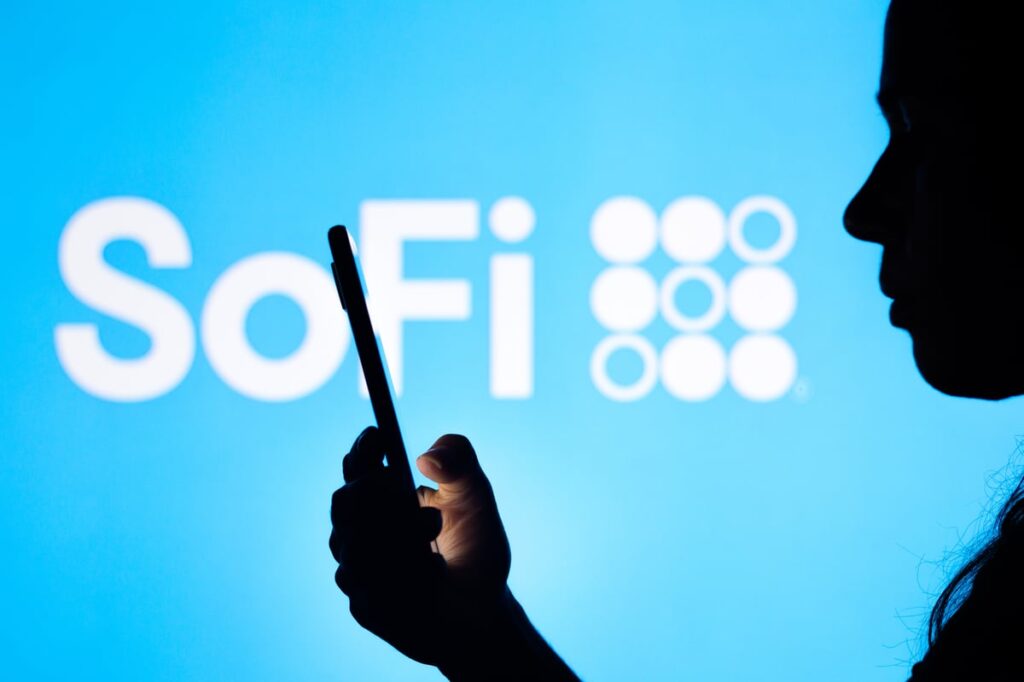 SoFi's logo is displayed behind a person looking at a smartphone.