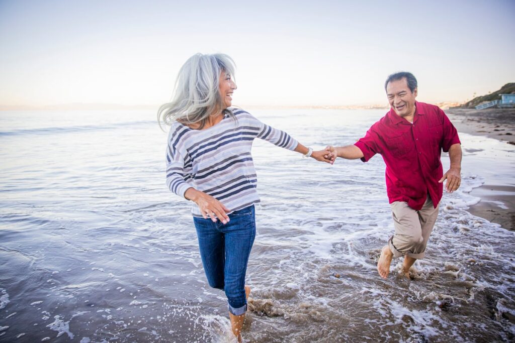 A retired couple runs along a beach.
