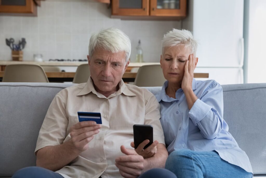 Two worried people sitting on sofa, looking at card and phone.