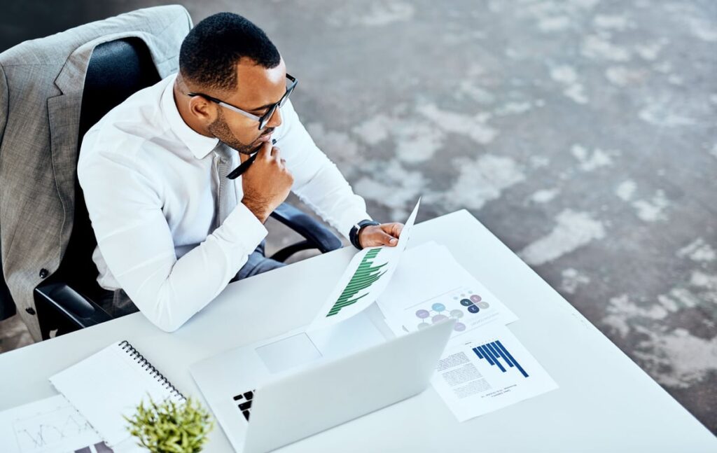 An investment analyst is sitting at a desk reviewing some printed documents.