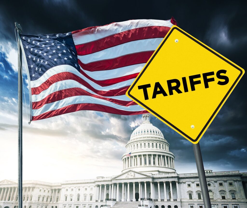 U.S. Capitol and flag in the background, with a bright yellow street sign reading "Tariffs" in the forefront.