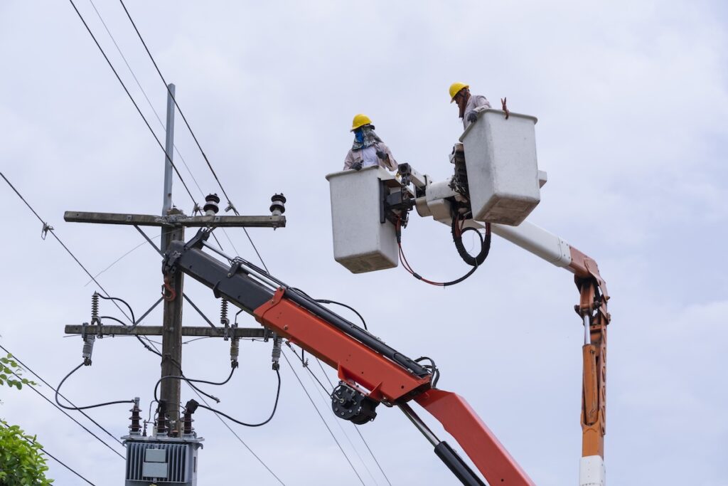 electrician works on bucket car to maintain high voltage transmission lines.
