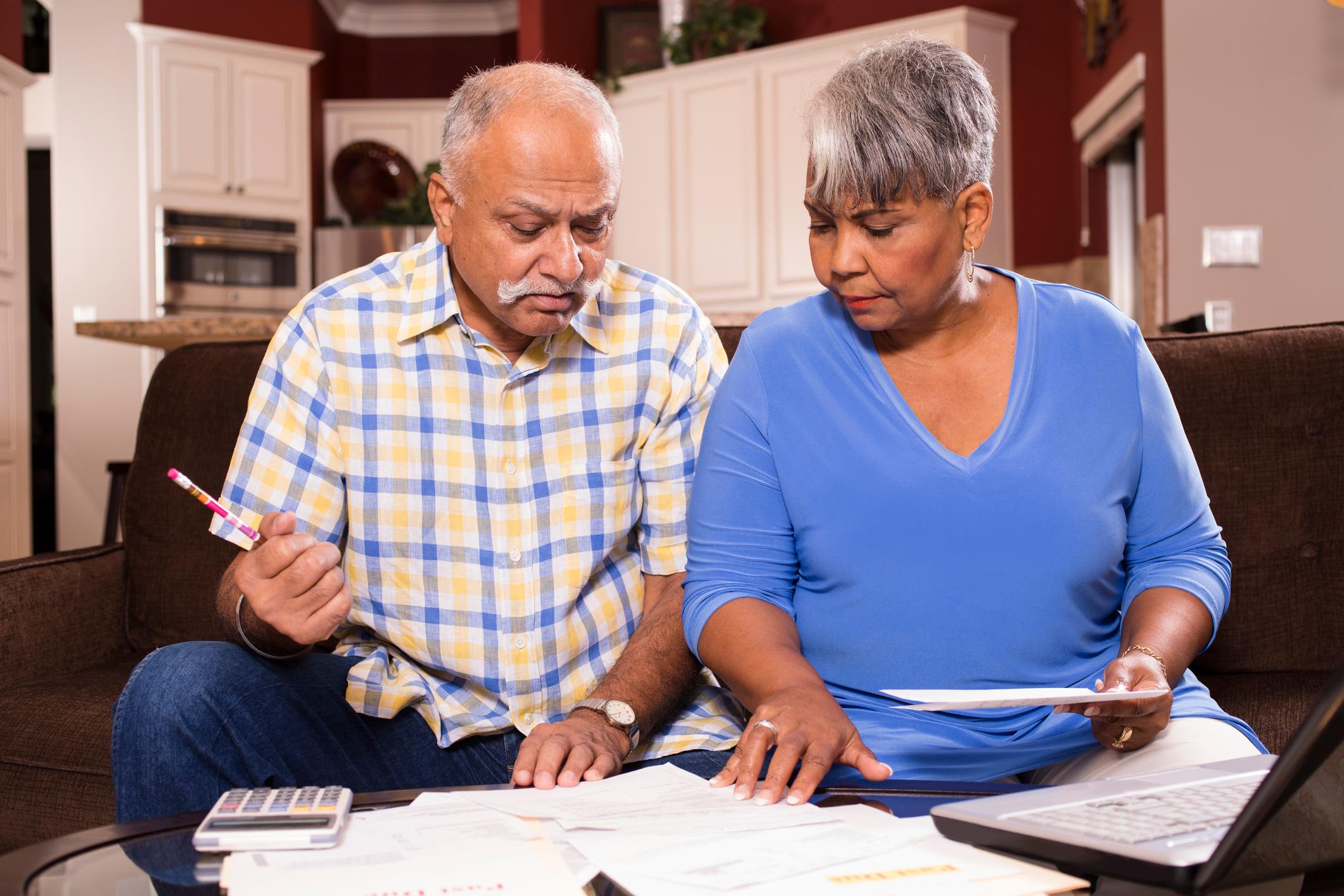A couple sitting on a couch, reviewing bills and finances set on a table in front of them.